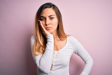 Young beautiful blonde woman with blue eyes wearing white t-shirt over pink background thinking looking tired and bored with depression problems with crossed arms.