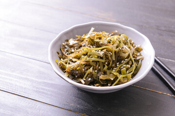 Bowl with tasty seaweed and chopsticks on wooden background
