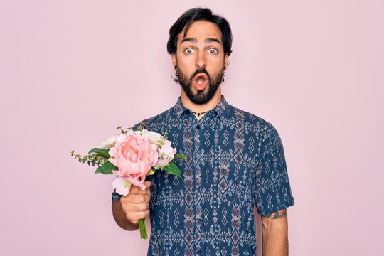 Young handsome hispanic bohemian hipster man with bear holding flowers bouquet scared in shock with a surprise face, afraid and excited with fear expression