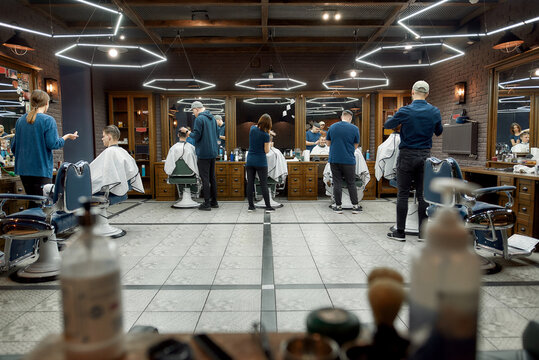 Barber team at work. Back view of several professional barbers working with clients in the modern loft style barber shop. General view. Hairdresser services