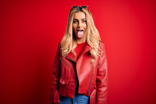 Young beautiful blonde woman wearing casual jacket standing over isolated red background sticking tongue out happy with funny expression. Emotion concept.