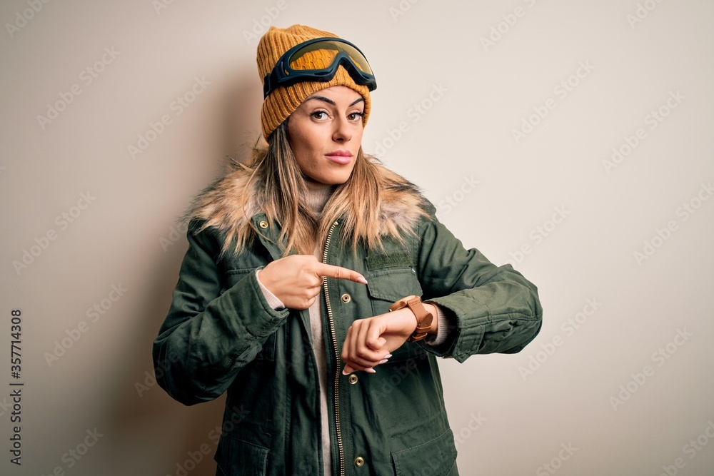 Canvas Prints Young brunette skier woman wearing snow clothes and ski goggles over white background In hurry pointing to watch time, impatience, upset and angry for deadline delay