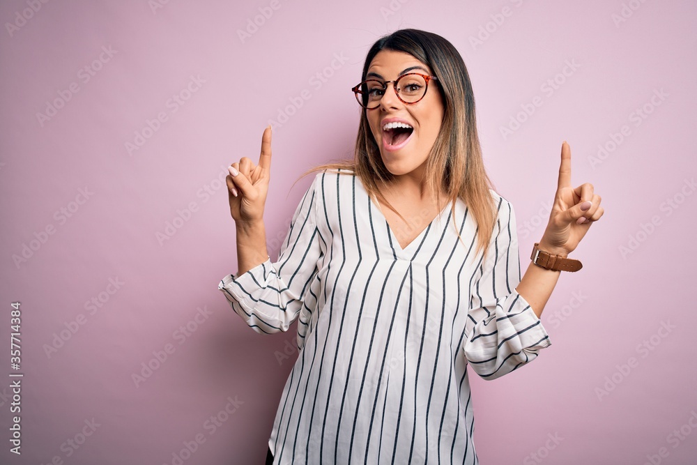 Wall mural young beautiful woman wearing casual striped t-shirt and glasses over pink background smiling amazed