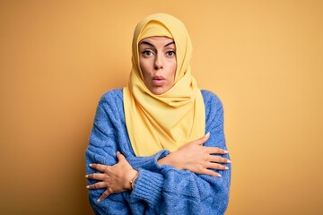 Young beautiful brunette muslim woman wearing arab hijab over isolated yellow background shaking and freezing for winter cold with sad and shock expression on face