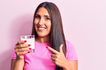 Fototapeta premium Young beautiful brunette woman drinking glass of milk smiling happy pointing with hand and finger