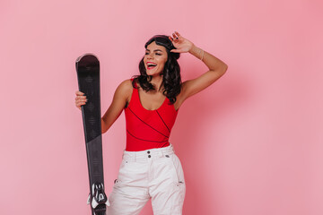 Inspired girl in white pants holding skis. Front view of glad tanned woman in sport goggles.