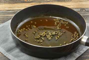 Brown sauce with capers in frying pan on dishtowel on table to add to dinner meal