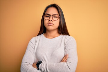 Young beautiful asian girl wearing casual sweater and glasses over yellow background skeptic and...