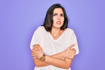 Young beautiful brunette woman wearing casual white t-shirt over purple background shaking and freezing for winter cold with sad and shock expression on face