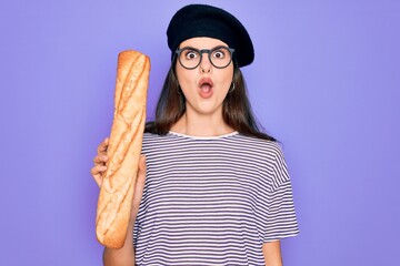 Young beautiful girl wearing fashion french beret holding fresh baked bread baguette scared in...