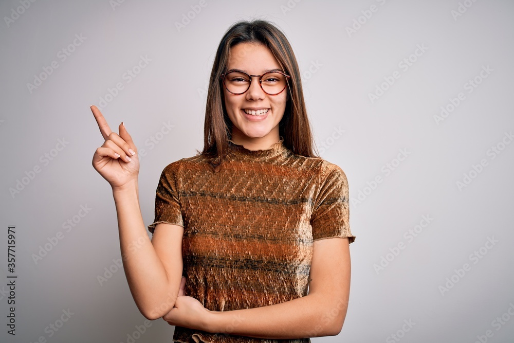 Wall mural young beautiful brunette girl wearing casual t-shirt and glasses over isolated white background with