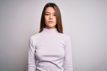 Young beautiful brunette girl wearing casual sweater standing over isolated white background with serious expression on face. Simple and natural looking at the camera.