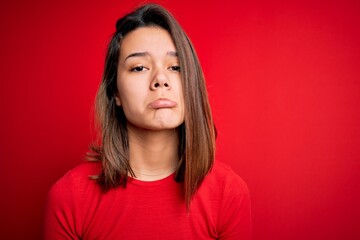 Young beautiful brunette girl wearing casual t-shirt over isolated red background depressed and worry for distress, crying angry and afraid. Sad expression.