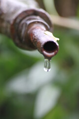 A drop of water dripping from a rusty tap.