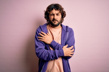 Fototapeta premium Young handsome sporty man with beard wearing casual sweatshirt over pink background shaking and freezing for winter cold with sad and shock expression on face
