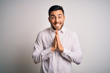Young handsome man wearing elegant shirt standing over isolated white background praying with hands together asking for forgiveness smiling confident.