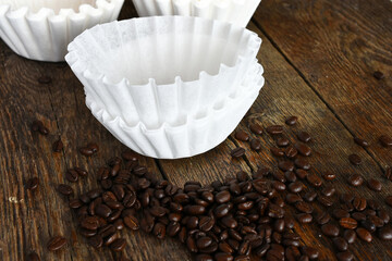 An image of several white basket style coffee filers and dark roasted coffee beans. 