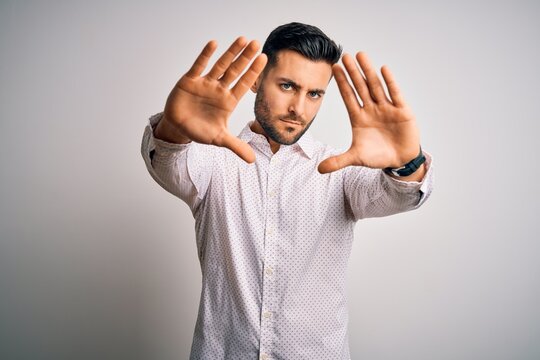 Young handsome man wearing elegant shirt standing over isolated white background doing frame using hands palms and fingers, camera perspective