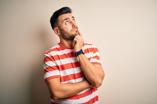 Young handsome man wearing casual striped t-shirt standing over isolated white background Thinking worried about a question, concerned and nervous with hand on chin