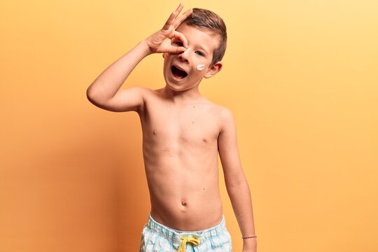 Cute blond kid wearing swimwear smiling happy doing ok sign with hand on eye looking through fingers