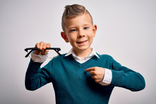 Young little caucasian kid holding eyesight glasses correction over isolated background with surprise face pointing finger to himself