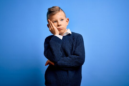 Young little caucasian kid with blue eyes wearing winter sweater over blue background thinking looking tired and bored with depression problems with crossed arms.