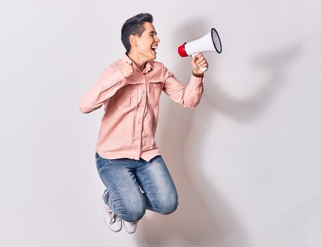 Young beautiful caucasian woman screaming using megaphone. Jumping over isolated white background