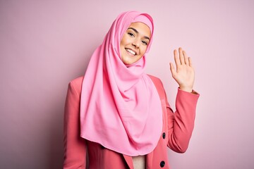 Young beautiful girl wearing muslim hijab standing over isolated pink background Waiving saying...