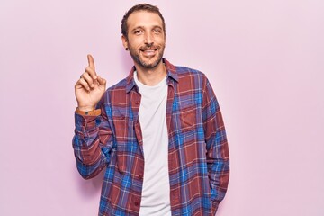 Fototapeta premium Young handsome man wearing casual clothes smiling with an idea or question pointing finger up with happy face, number one