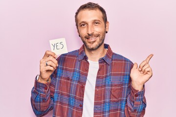 Young handsome man holding yes reminder smiling happy pointing with hand and finger to the side
