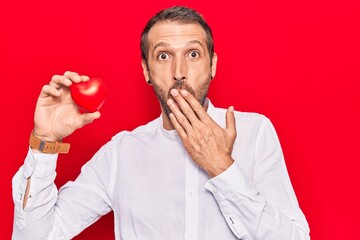 Young handsome man holding heart covering mouth with hand, shocked and afraid for mistake....