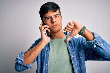Young handsome man having conversation talking on the smartphone over white background with angry face, negative sign showing dislike with thumbs down, rejection concept