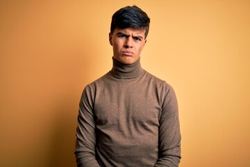 Young handsome man wearing casual turtleneck sweater over isolated yellow background skeptic and...