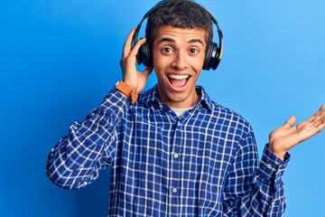 Young african amercian man listening to music using headphones celebrating achievement with happy smile and winner expression with raised hand