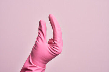 Hand of caucasian young man with cleaning glove over isolated pink background picking and taking invisible thing, holding object with fingers showing space