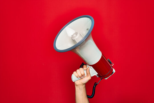 Beautiful hand of man holding megaphone over isolated red background