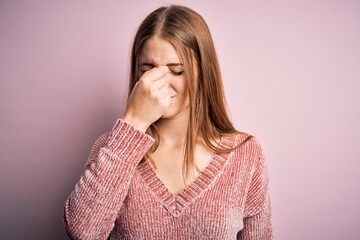 Young beautiful redhead woman wearing casual sweater over isolated pink background tired rubbing nose and eyes feeling fatigue and headache. Stress and frustration concept.