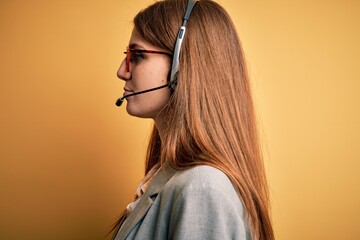 Young redhead call center agent woman overworked wearing glasses using headset looking to side,...