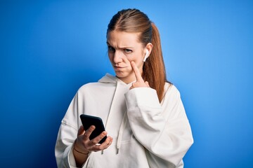 Young redhead sportswoman doing sport listening to music using earphones and smartphone Pointing to the eye watching you gesture, suspicious expression