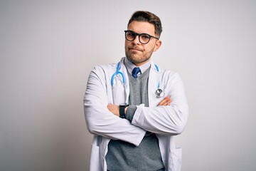 Young doctor man with blue eyes wearing medical coat and stethoscope over isolated background skeptic and nervous, disapproving expression on face with crossed arms. Negative person.