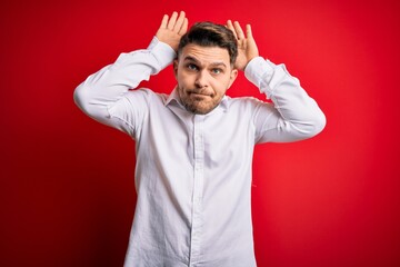 Young business man with blue eyes wearing elegant shirt standing over red isolated background Doing...