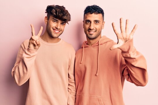 Young gay couple wearing casual clothes showing and pointing up with fingers number seven while smiling confident and happy.