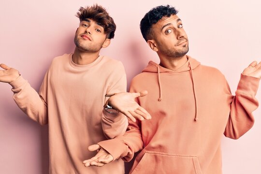 Young gay couple wearing casual clothes clueless and confused expression with arms and hands raised. doubt concept.