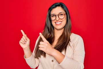 Young hispanic smart woman wearing glasses standing over red isolated background smiling and looking at the camera pointing with two hands and fingers to the side.