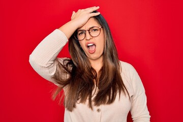 Young hispanic smart woman wearing glasses standing over red isolated background surprised with...
