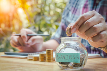 Young businessman writing receipts Expenditure into notebooks and putting coins in piggy banks to save money invest for future.