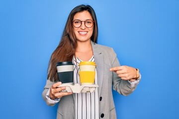 Young hispanic intern business woman holding coffee over blue background very happy pointing with...