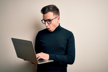 Young handsome caucasian business man wearing glasses using computer laptop scared in shock with a surprise face, afraid and excited with fear expression