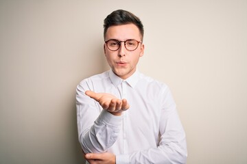 Young handsome business mas wearing glasses and elegant shirt over isolated background looking at the camera blowing a kiss with hand on air being lovely and sexy. Love expression.