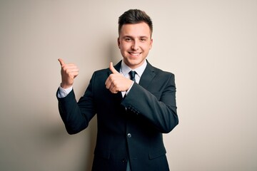 Young handsome business man wearing elegant suit and tie over isolated background Pointing to the back behind with hand and thumbs up, smiling confident